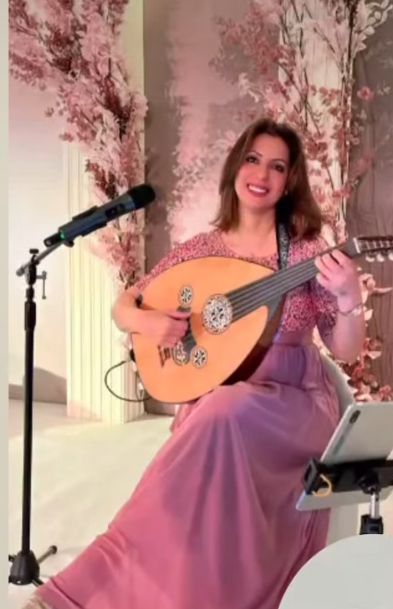 Nina Oud singing and playing the oud on a floral stage